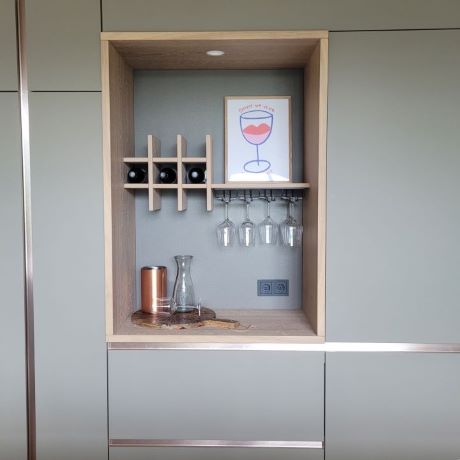 Nis in luxe maatwerkkeuken. Eiken handgemaakte wijnrek met hangende glazen. Matte fronten en messing greeplijsten
